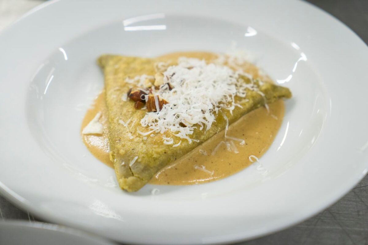 Close-up of a savory crepe topped with grated cheese and sauce, served on a white plate.