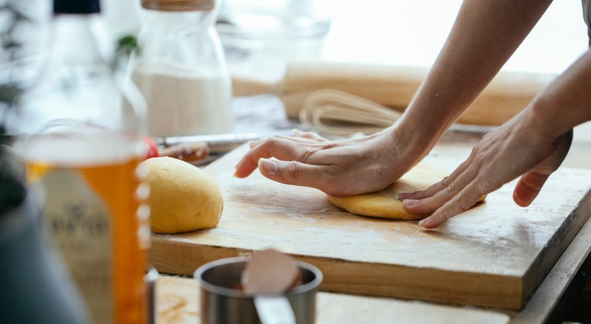Female hands kneading fresh dough on wooden chopping board with flour in kitchen